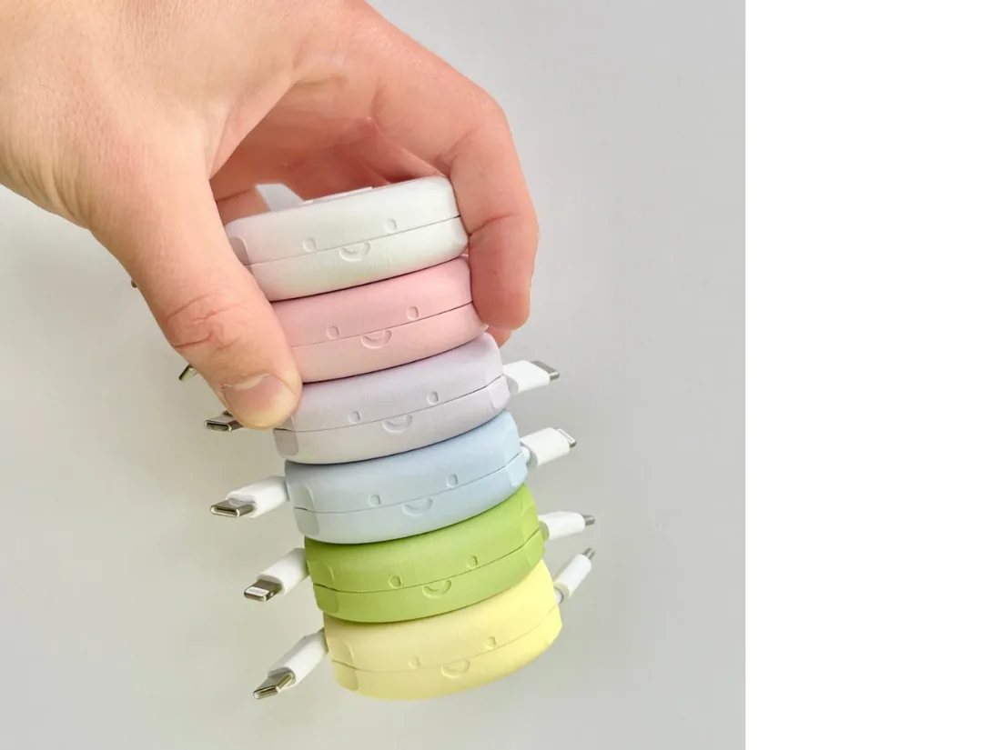 Stack of pastel-coloured 3D-printed branded containers in pink, blue, lavender, green and yellow, held in a hand