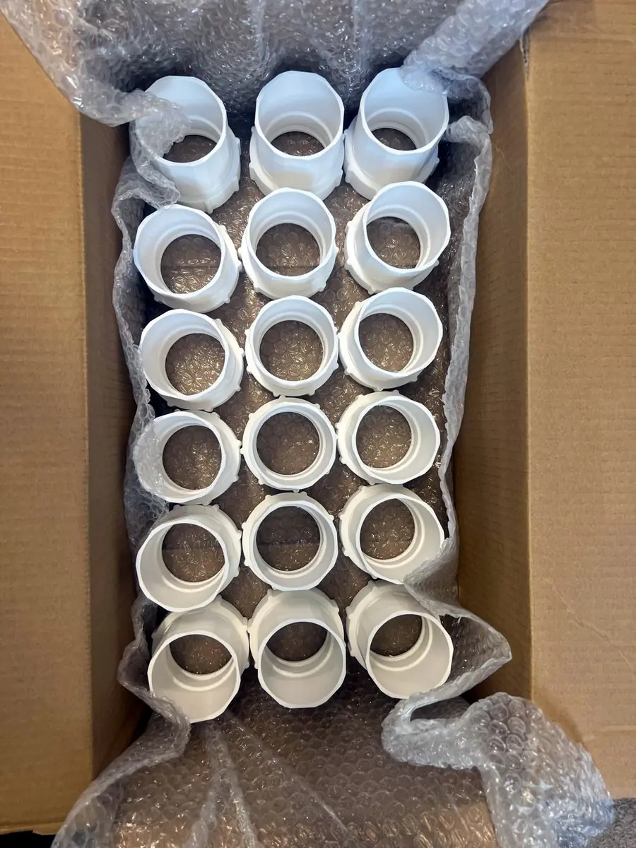 Overhead view of an open box of 3D printed couplers with their nuts fitted, in bubble wrap. 18 are visible; the full run was 40 of each.