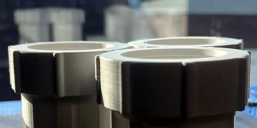 Three white 3D printed couplers with ribbed nuts fitted on the printer plate, against a blue sky