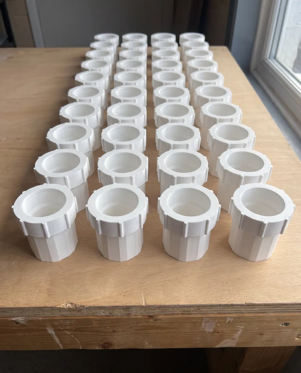 AI-made image of the full run: 40 white 3D printed couplers with their nuts fitted, lined up in four columns and ten rows on a wooden workshop table