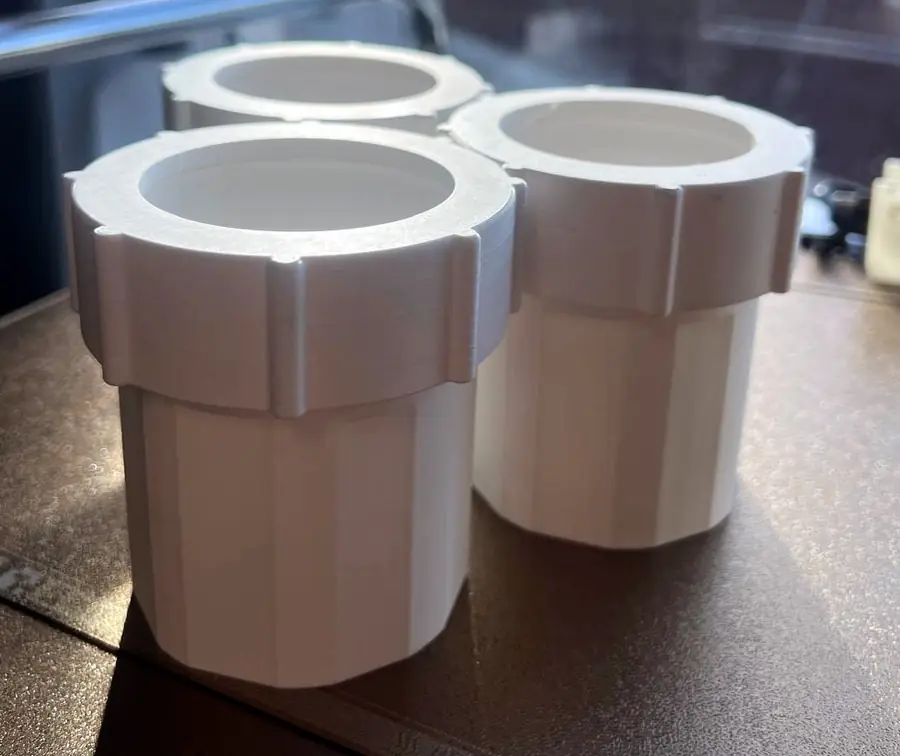 Close view of white 3D printed couplers with their ribbed nuts fitted, standing on the printer plate by a window