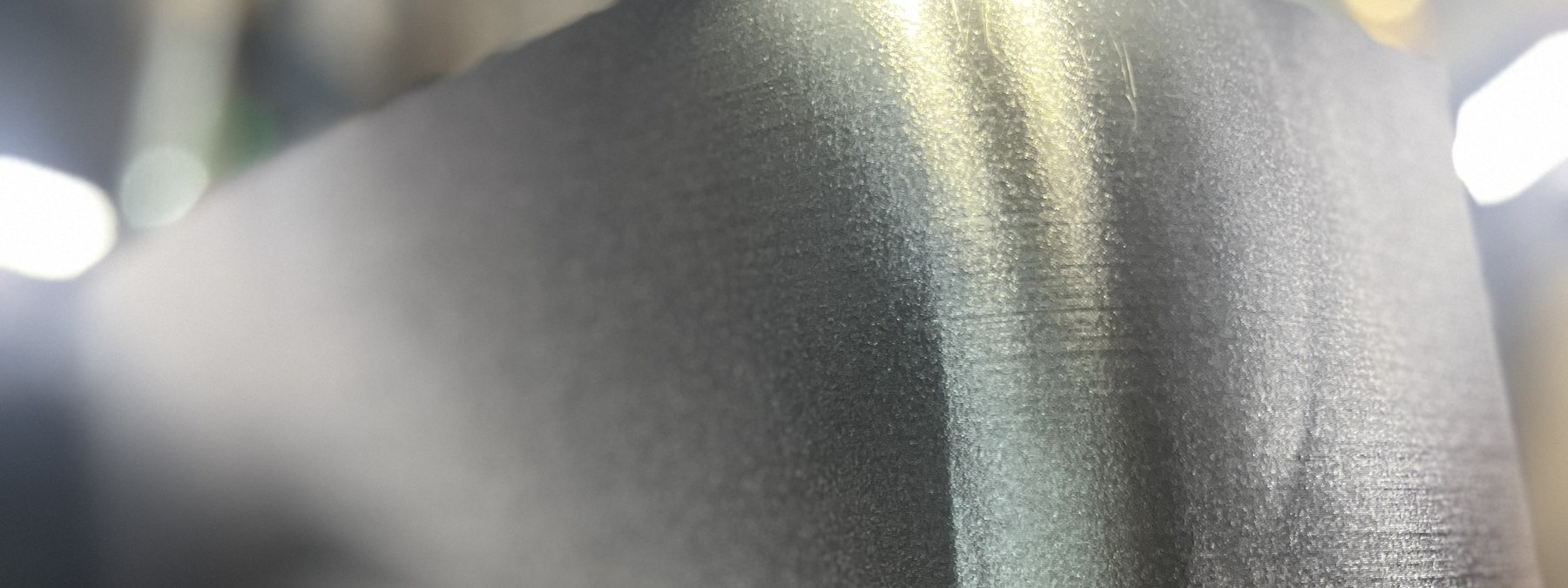 Sharp macro of a black PA12 part being printed mid-process, crisp layer texture catching the workshop light