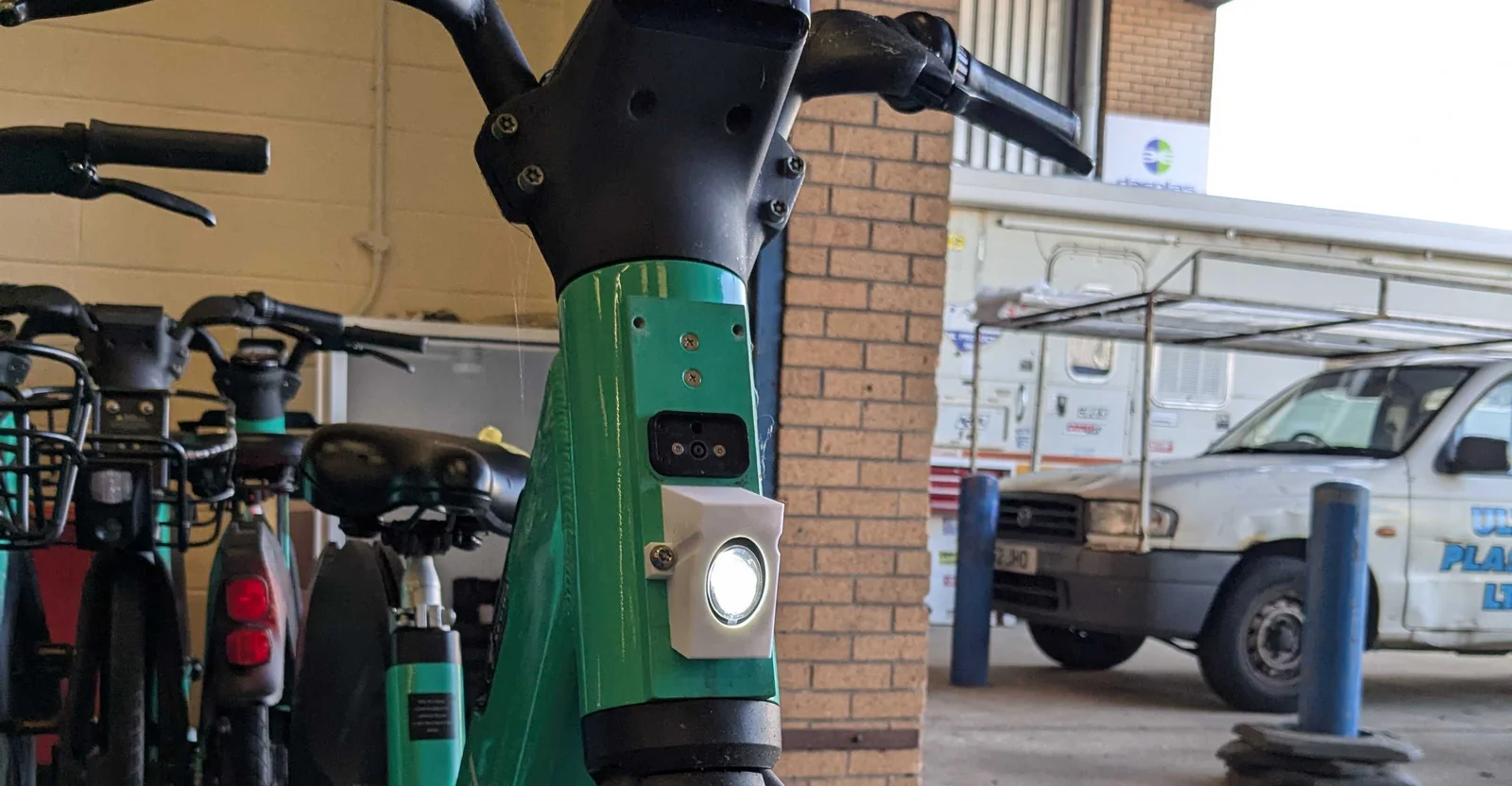 A Beryl shared e-bike with the 3D-printed front-light mount fitted to its head stem, LED lit, among the fleet at the depot