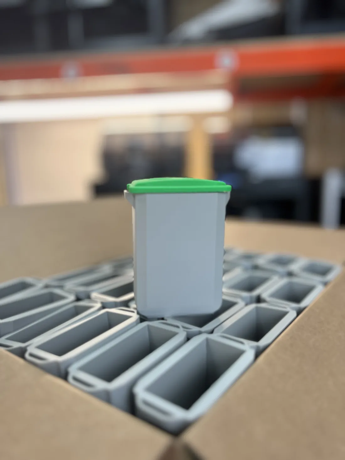A finished grey and green 3D printed mini DURABIN desk pen pot standing on rows of the batch at the 3D Printing Express workshop in Poole
