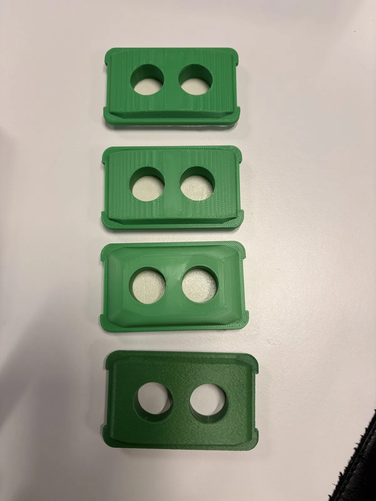 Four green 3D printed DURABIN lids on a white surface, each with two holes for pens