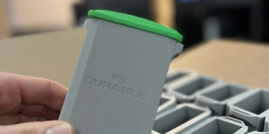 Durable case study · a real DURABLE-branded grey 3D-printed bin with a green snap-lid, held over a box of identical bins in the 3DPE workshop