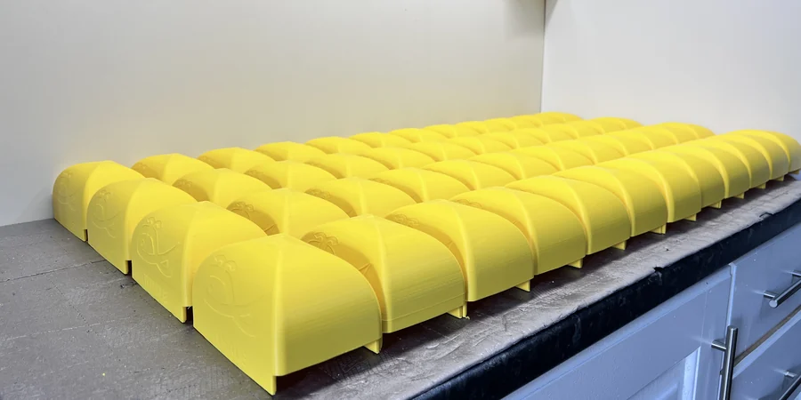 Whale Tankers case study · a real batch of identical WHALE-branded bright-yellow 3D-printed parts laid out in rows on the 3DPE workshop bench