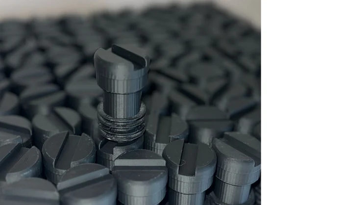 Macro photo of a 3DPE batch run · dense field of identical small black knobs printed and laid out for QC
