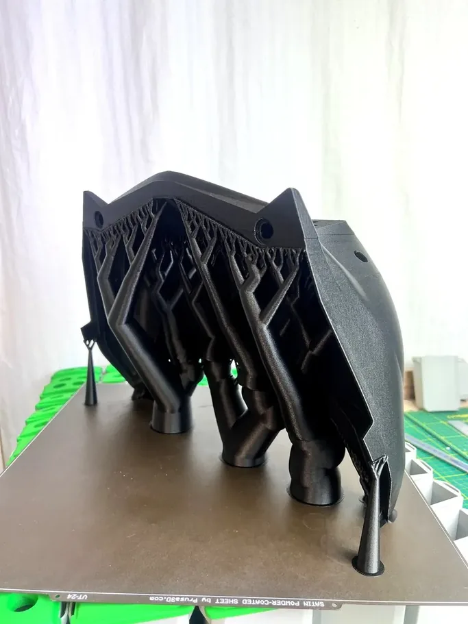 Large dark grey 3D-printed shell with a visible internal lattice structure for stiffness on a Prusa XL print bed