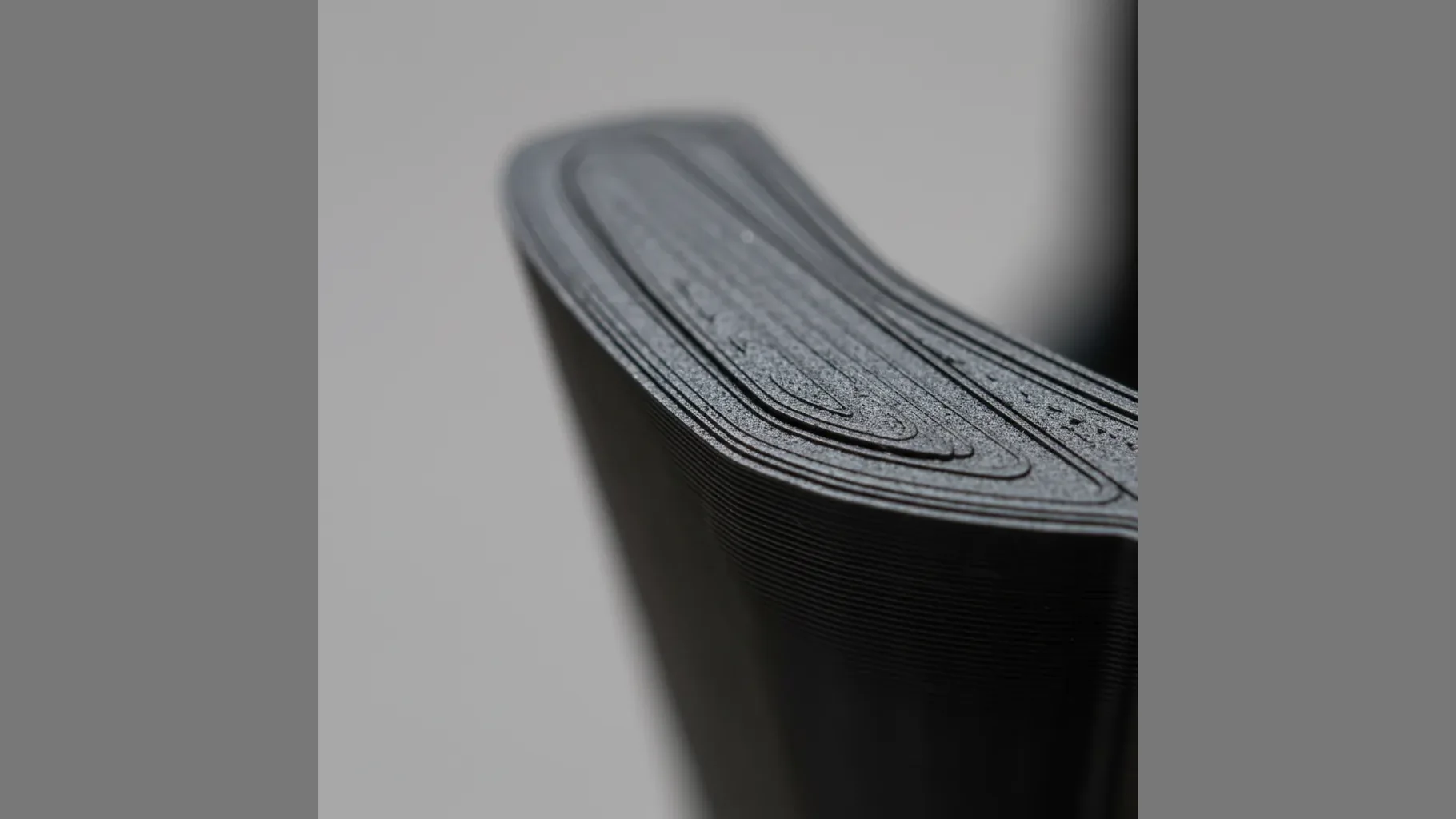 Extreme macro of a 3D-printed PC-ABS part surface showing fine layer lines and a smooth semi-matte black finish