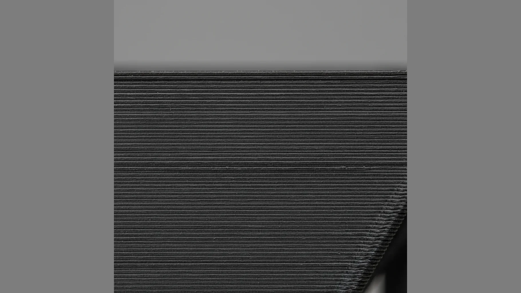 Extreme macro of the surface of a matte black 3D-printed PA12-CF part showing speckled chopped carbon-fibre flecks and fine layer lines