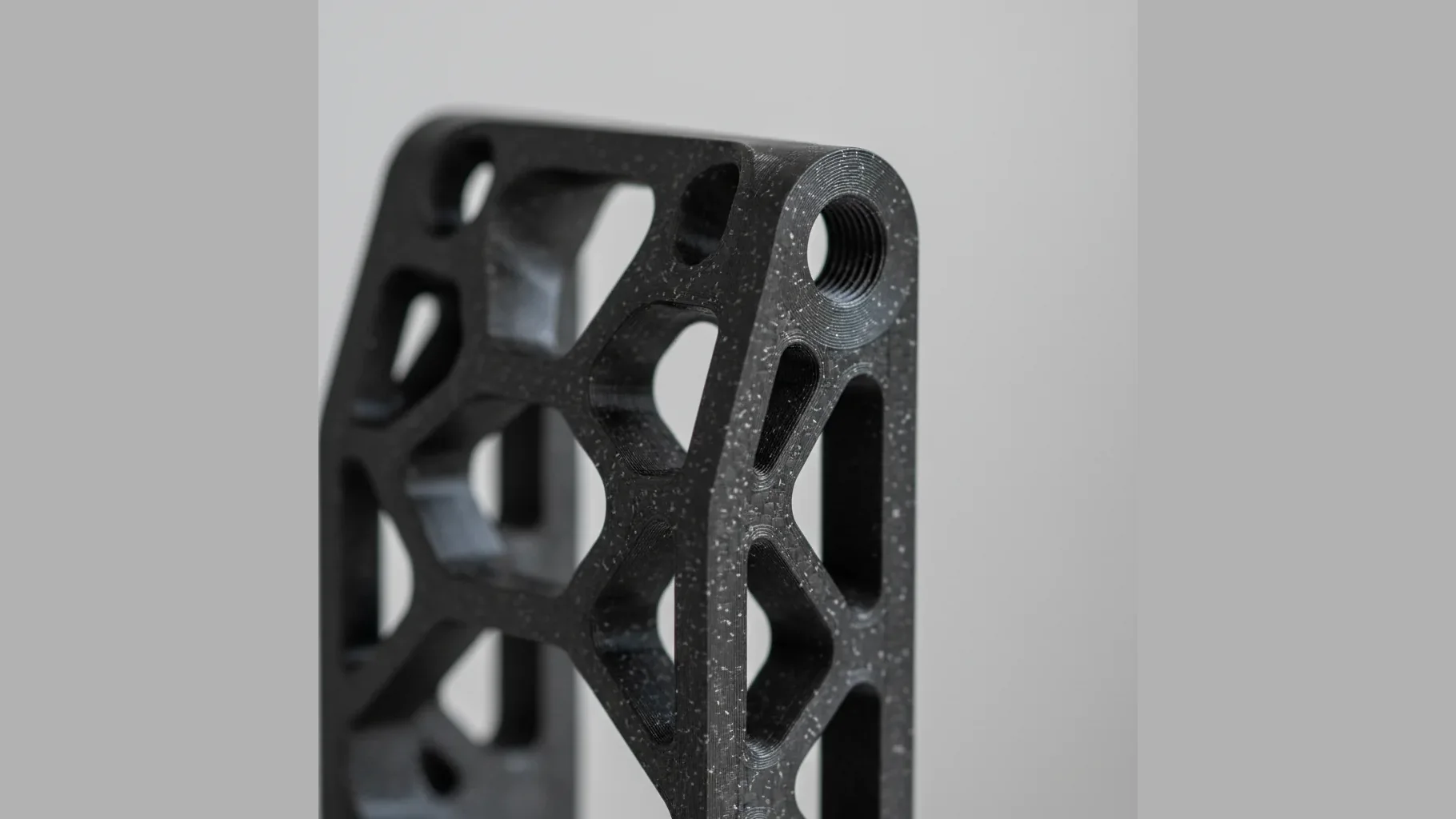 A single matte black 3D-printed PA12-CF structural bracket with precise bolt holes