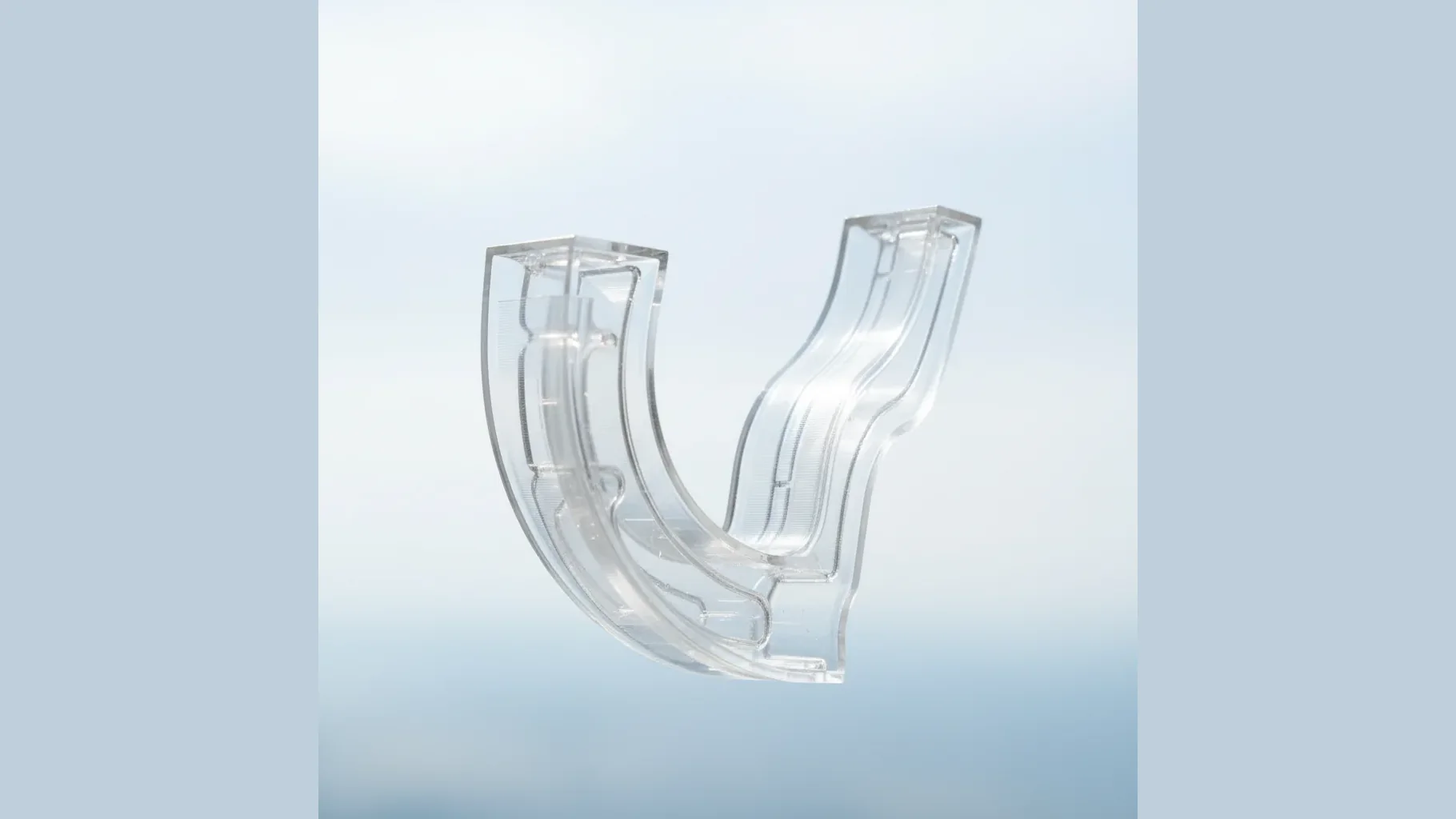 A clear transparent 3D-printed polycarbonate part held to soft light showing its optical clarity