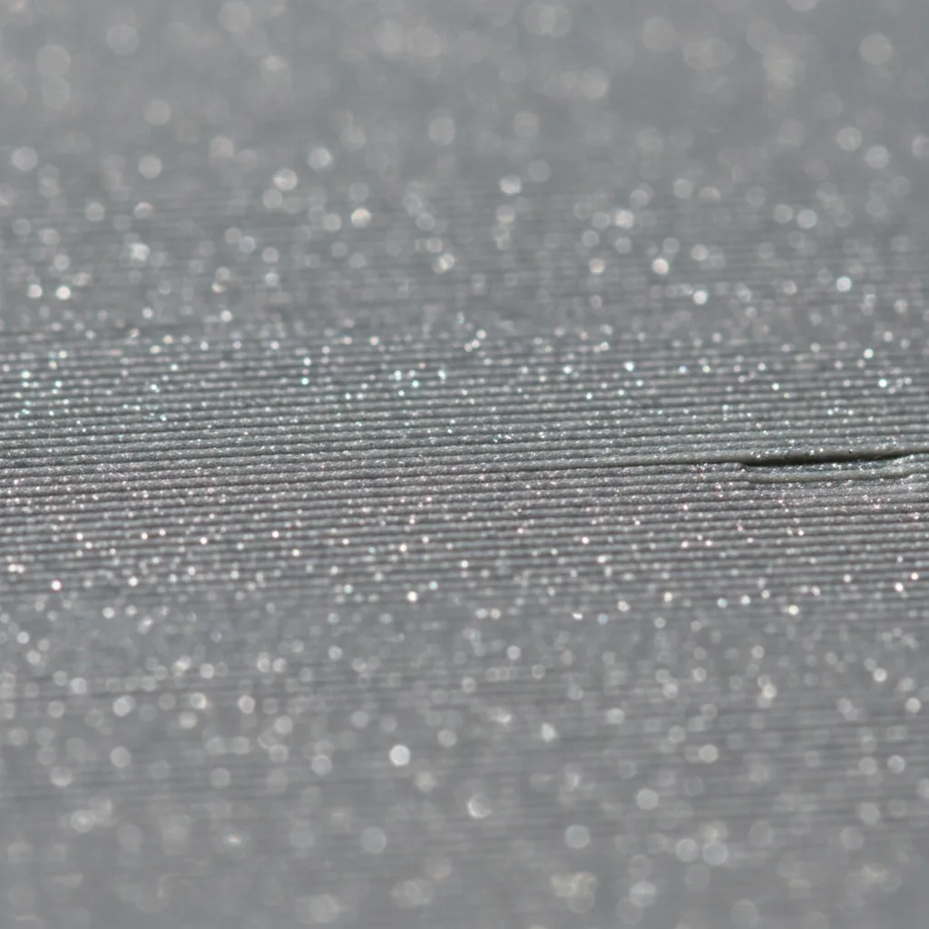 Extreme macro of the surface of a matte grey 3D-printed PET-GF part: fine sparkling glass-fibre speckle catching the light