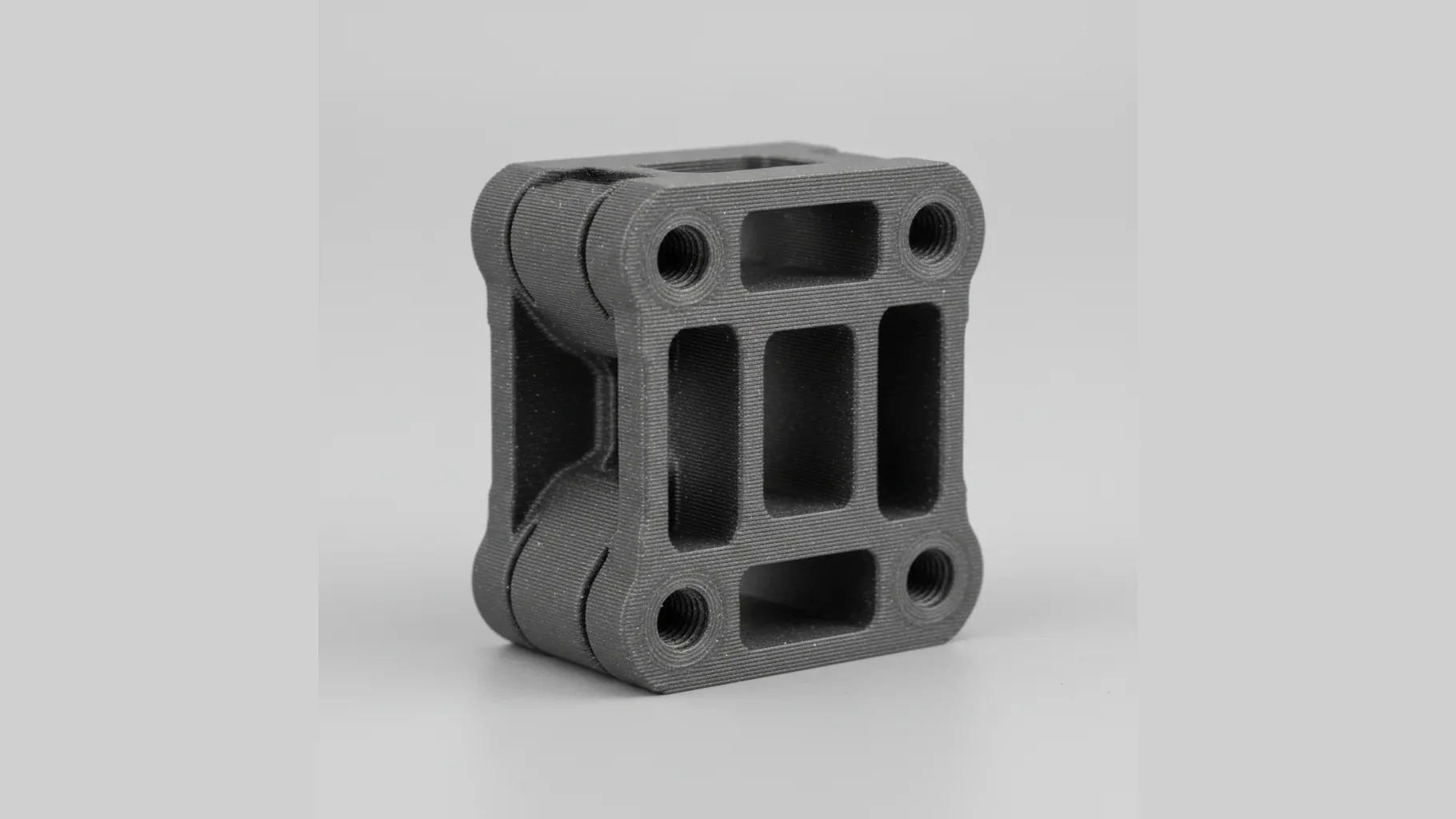 A single matte grey 3D-printed PET-GF structural bracket with precise bolt holes