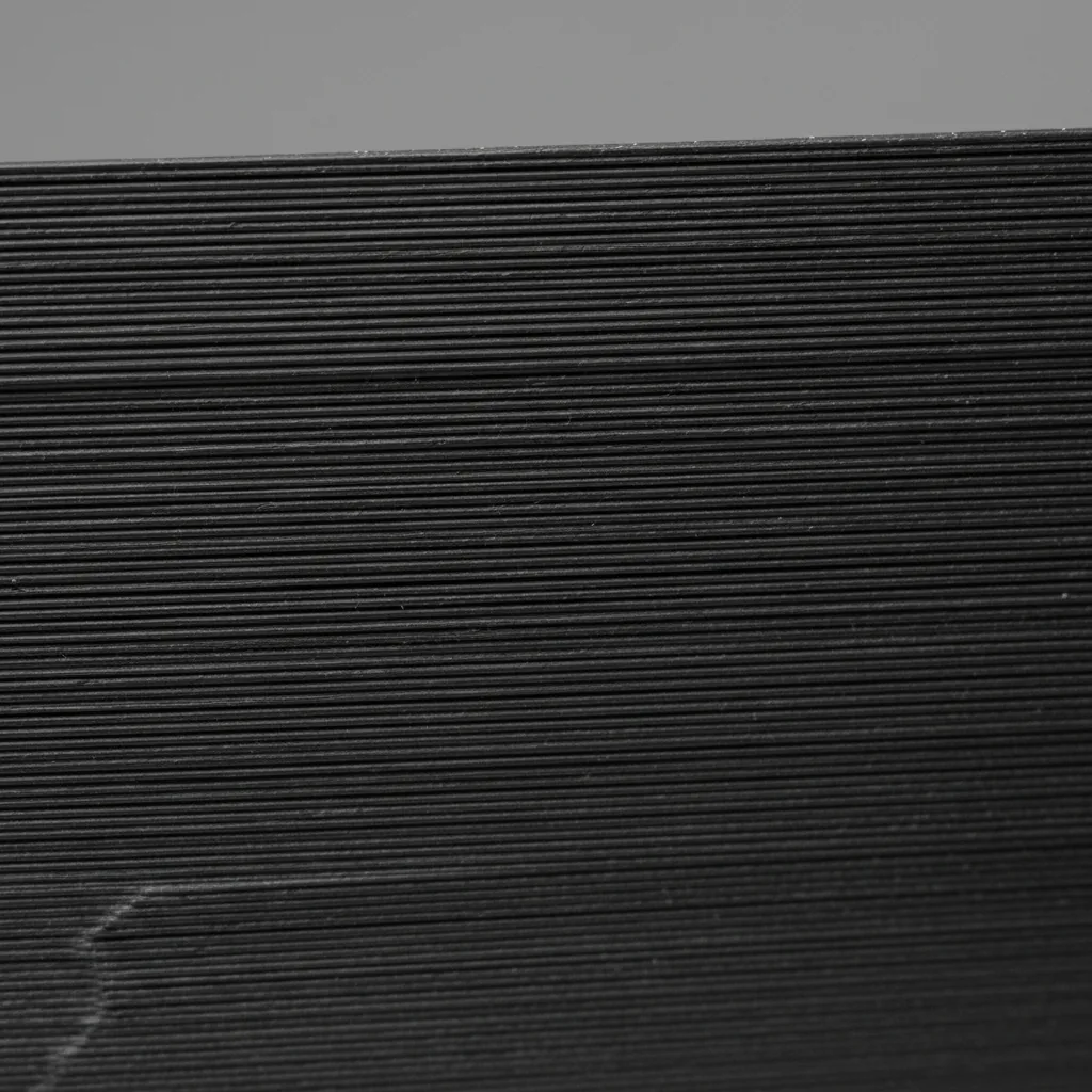Extreme macro of the surface of a deep matte black 3D-printed PPS-CF part: uniform fine matte carbon texture with clearly visible horizontal layer lines and a subtle satin sheen
