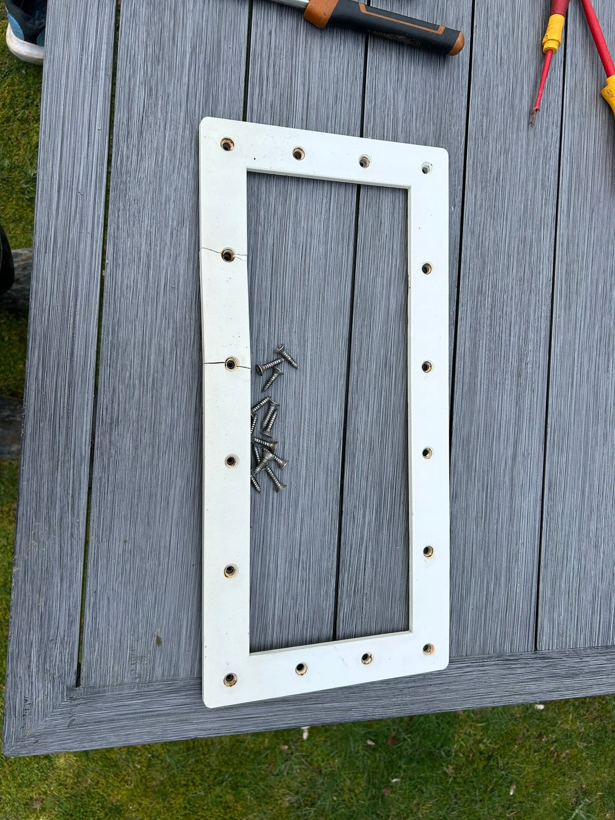 The real cracked Pooltec pool-skimmer front plate on a bench with its fixing screws · the original obsolete part we reverse-engineered