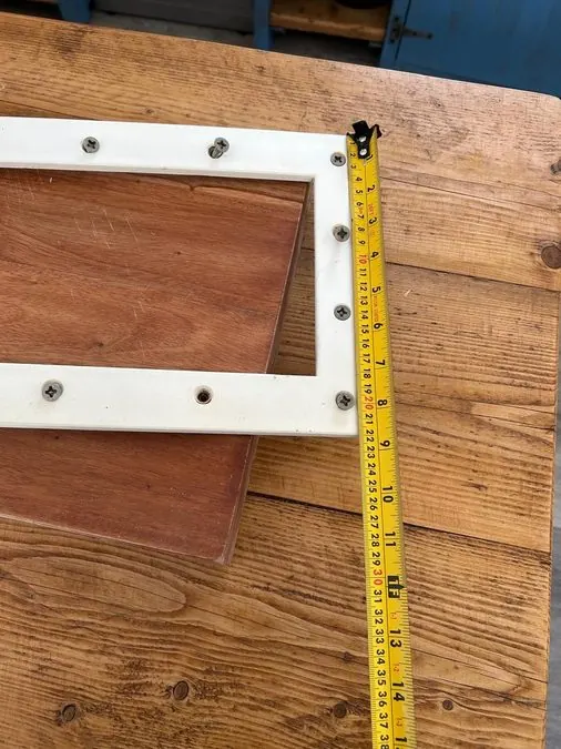 A real client-supplied photo · the original Pooltec skimmer plate on a workshop bench with a tape measure showing dimensions