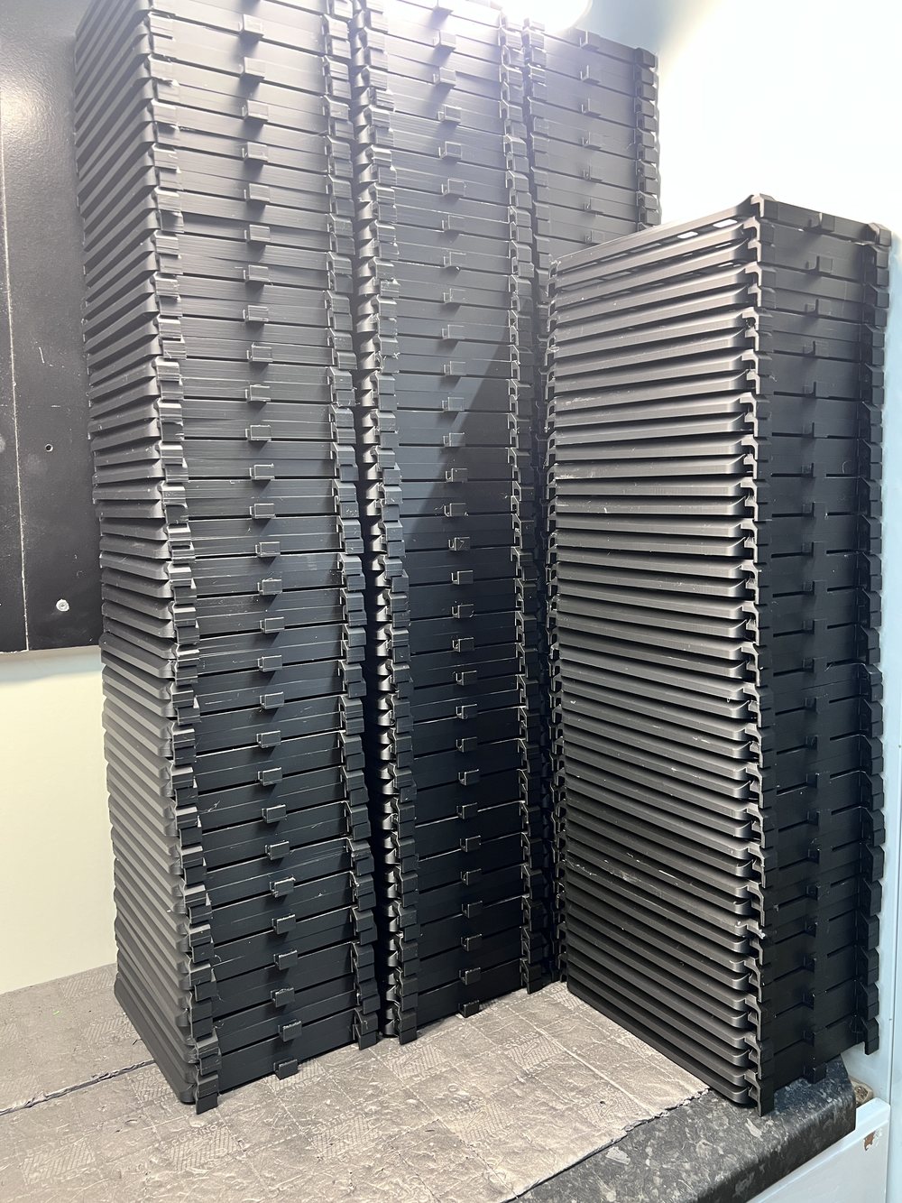 Stacks of identical 3D-printed black bird-cage door parts from the 1,000-unit production run