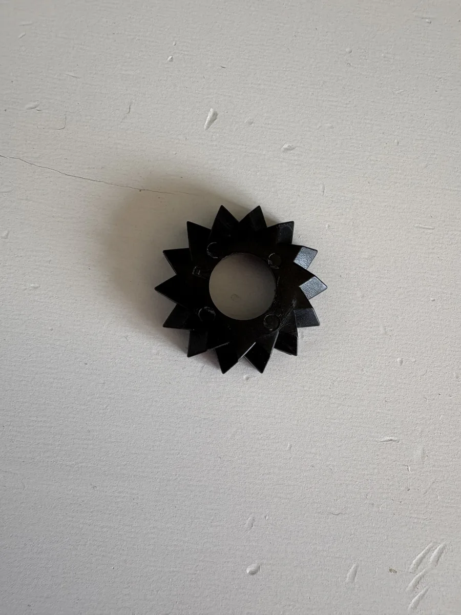 A small black plastic pram fold-mechanism cog next to a fold-out hinge