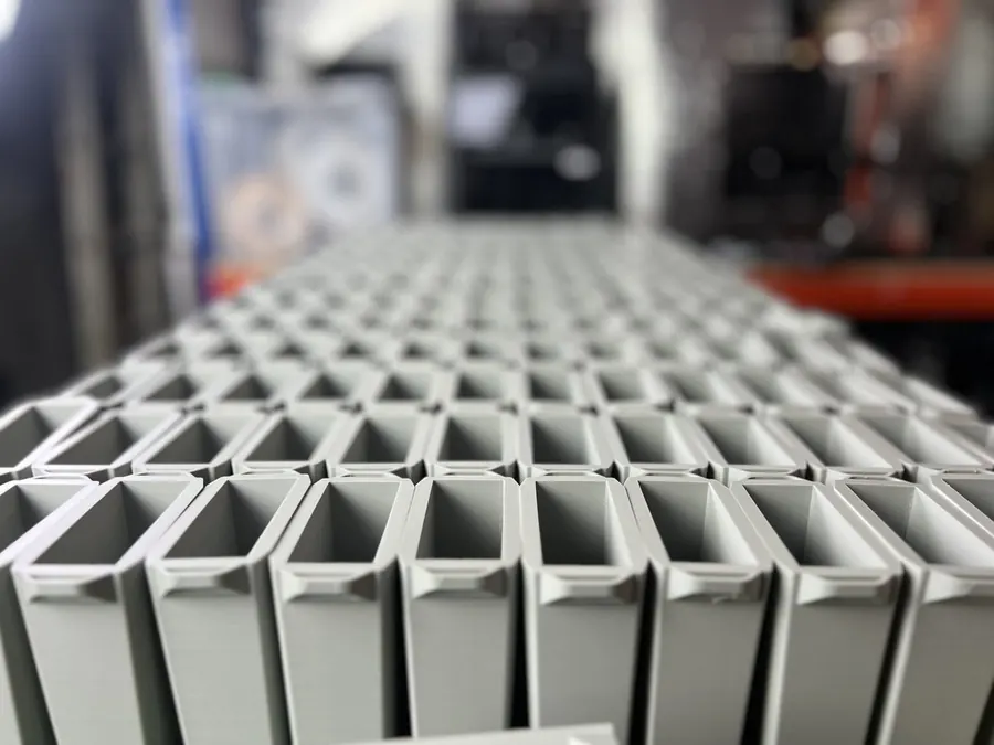 3DPE small-batch production · grid of identical grey hollow rectangular bins · consistent tolerance across the run